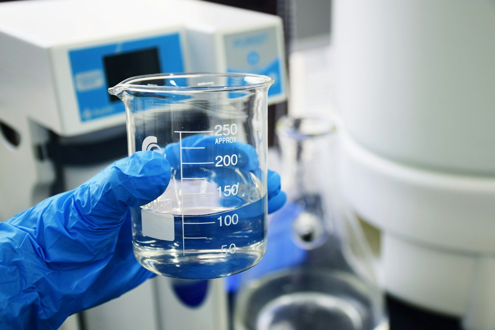 A gloved hand holding a glass beaker filled with clear liquid in a laboratory